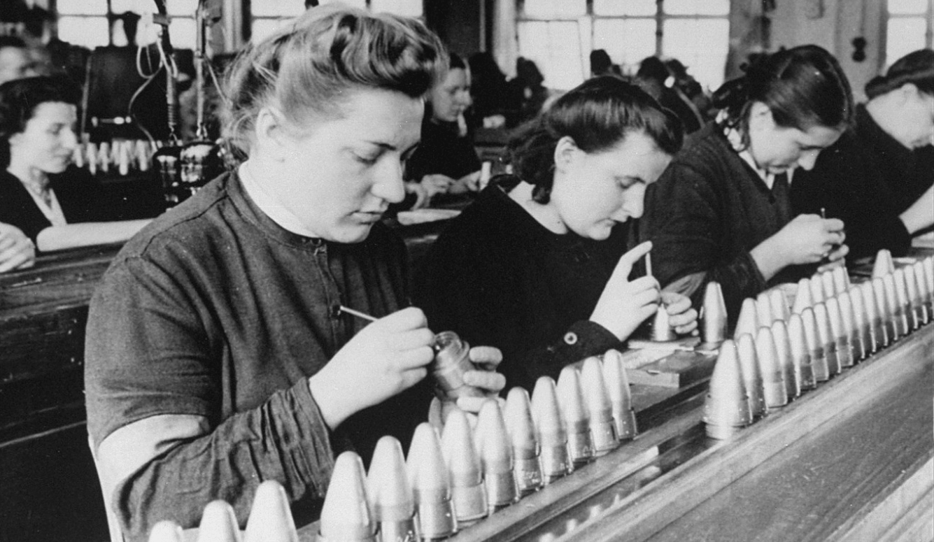 Women factory workers work on conical objects. Black-and-white photograph. 