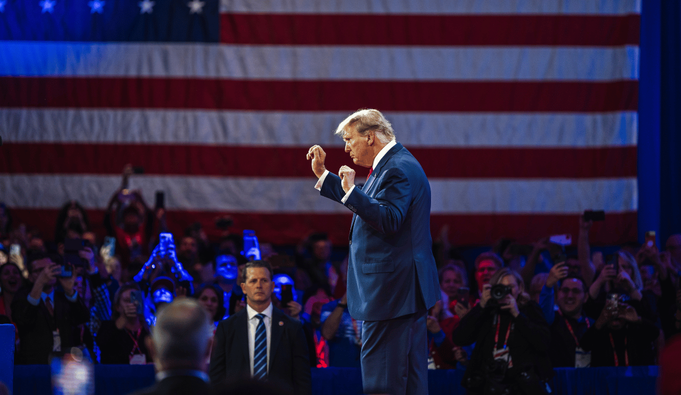 Donald Trump dancing on stage with his fists in the air, a huge American flag in the background.