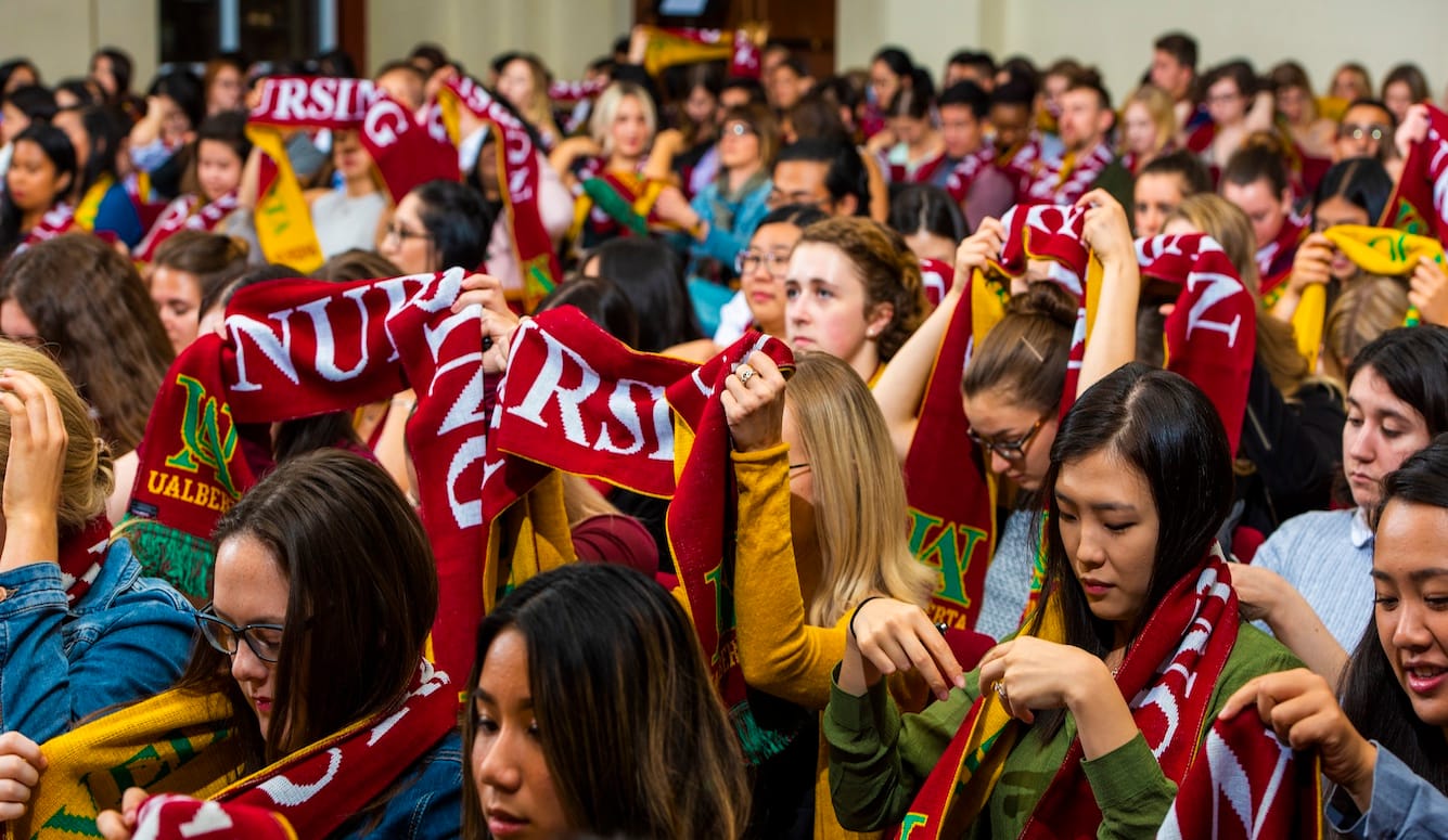 A group of women hold up their U of Alberta Nursing scarves. 