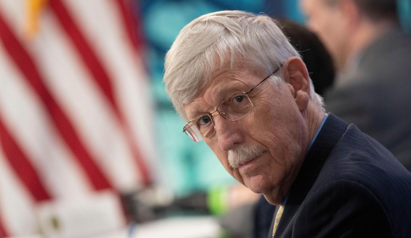 Francis Collins, an older man with grey hair and glasses, looks towards the camera. He wears a suit and tie. 