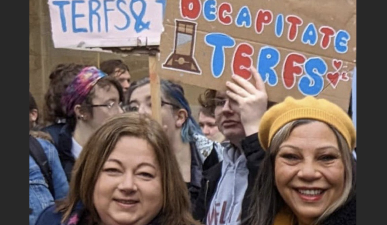 Protestors. One holds a banner saying, 'DECAPITATE TERFS.'