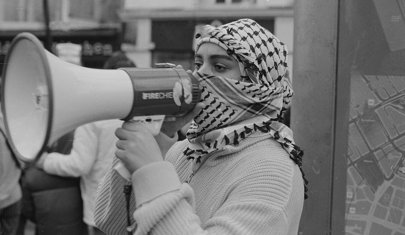 Young woman in keffiyeh shouts into megaphone.