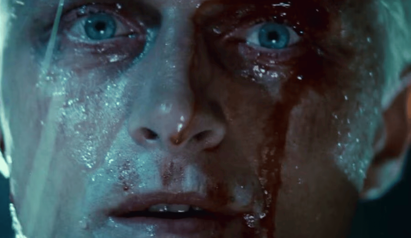 A close up of a blonde man with blue eyes in the rain.