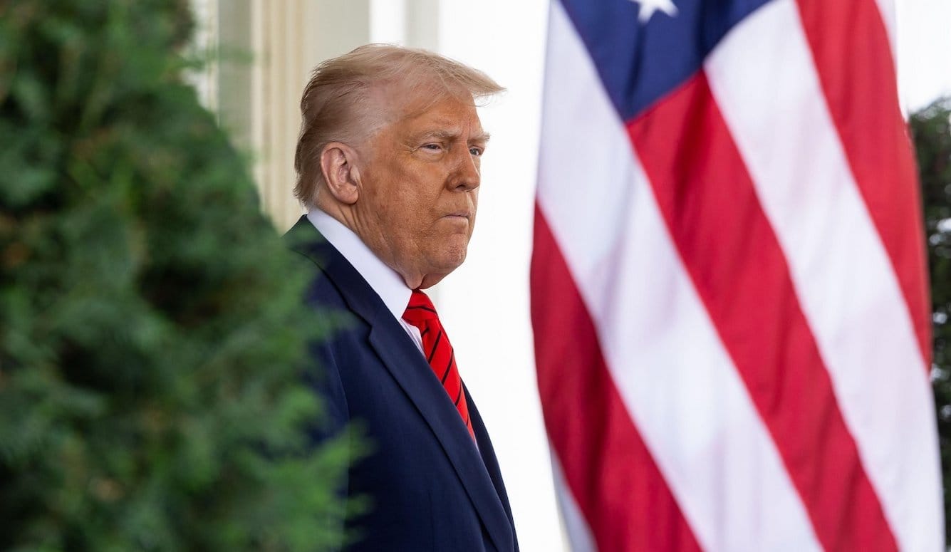 Donald Trump stands in front of an American flag.