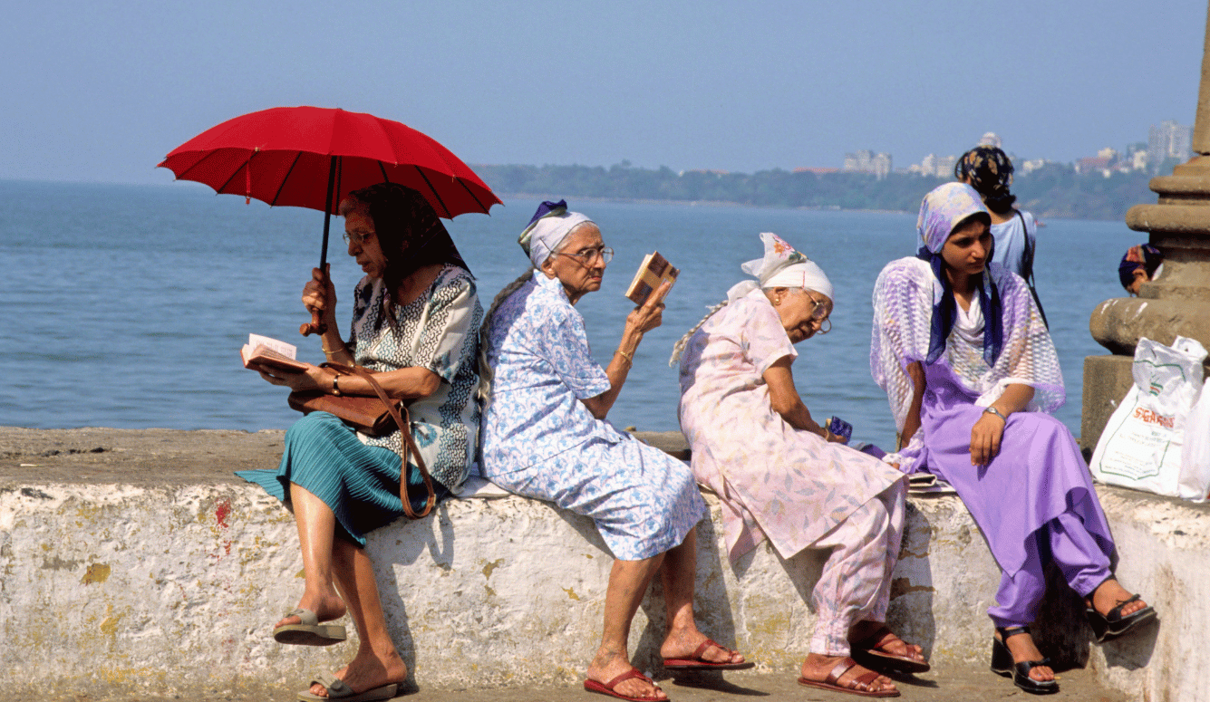 Parsi women praying at the sea wall in Bombay. They wear colourful clothes and headscarves.