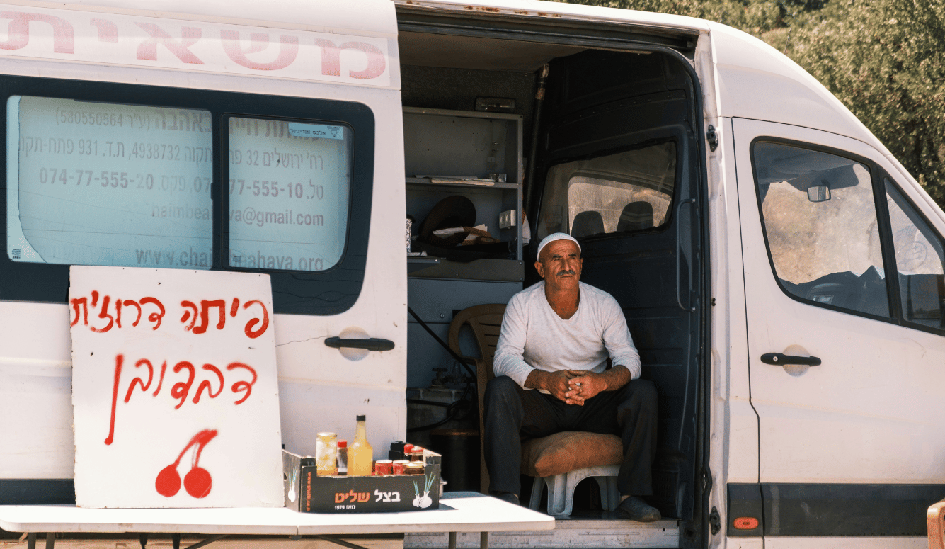  A Druse man sitting in front of local food truck of Pita and Cherries.
