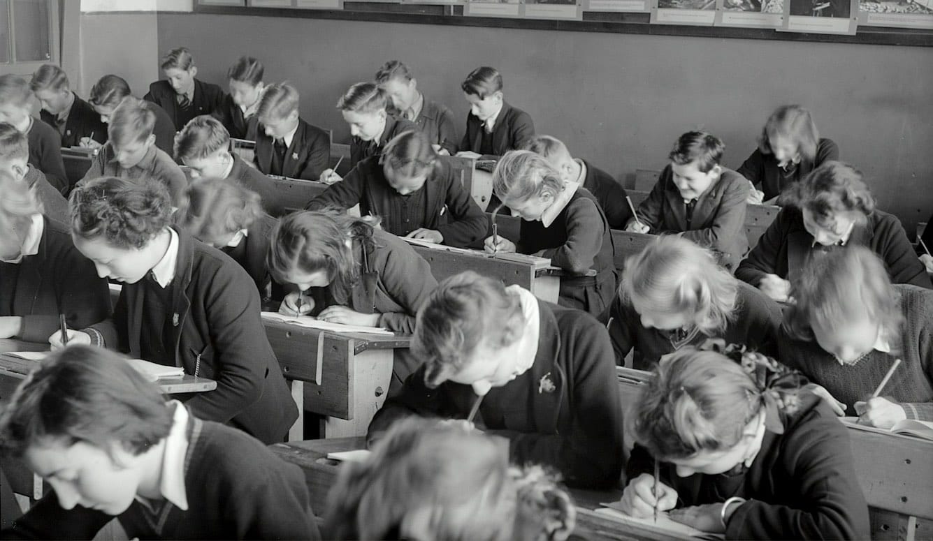 1950s black-andwhite image of students writing at their desks.
