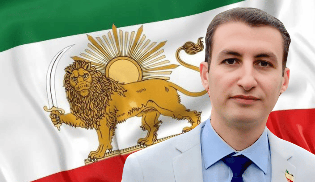 Danial Taghaddos in a grey suit and the flag of Imperial Iran, with a lion holding a sword and a sun.