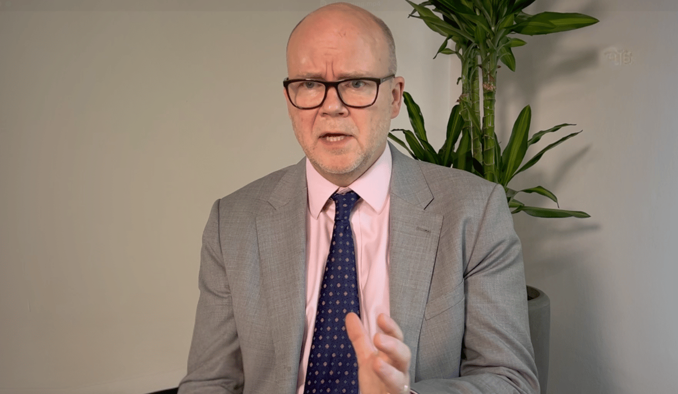 Toby Young is a white man in his fifties. He is bald, with glasses and wears a suit.  