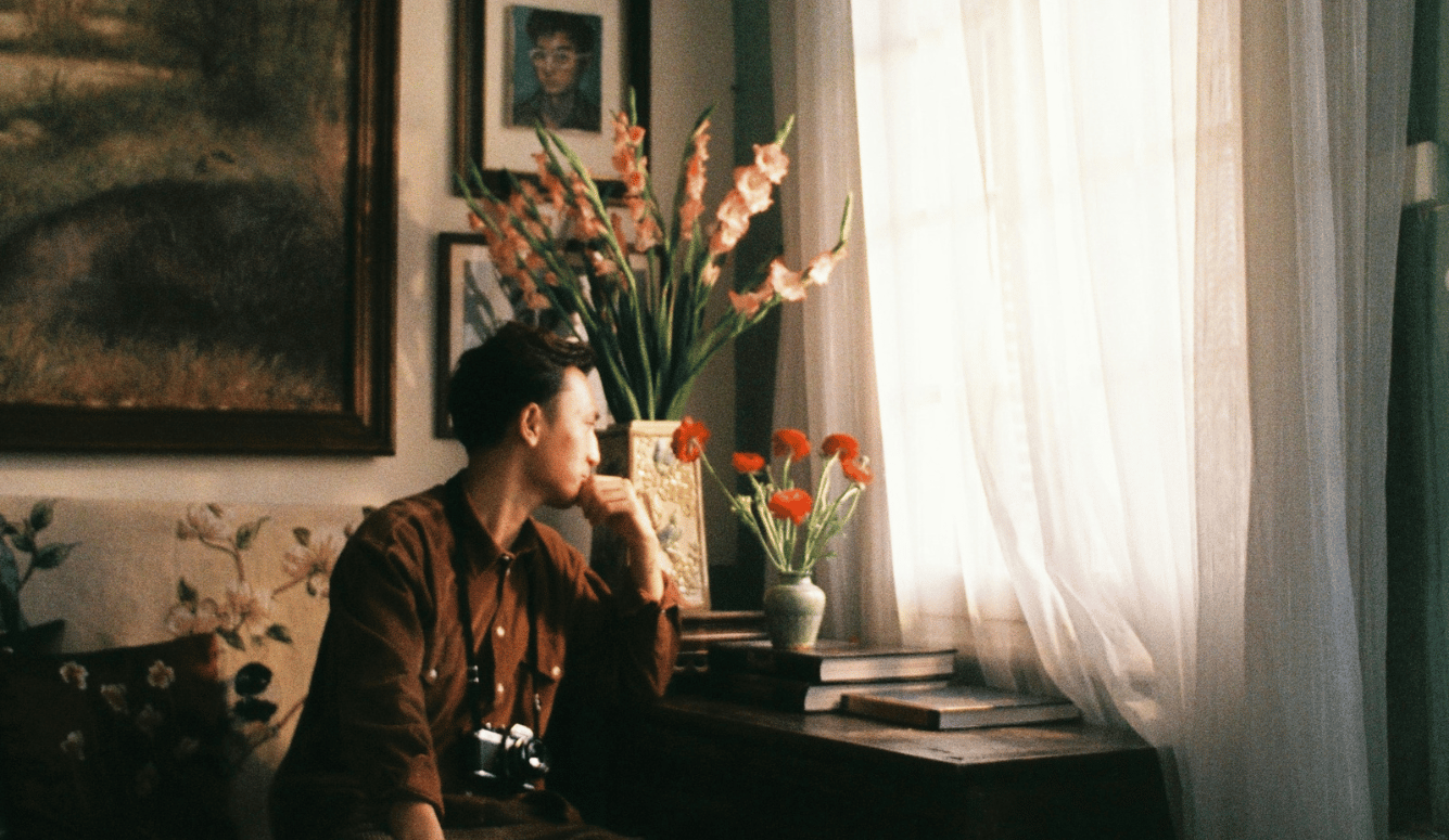 A man sitting on a couch in front of a window with flower vases.