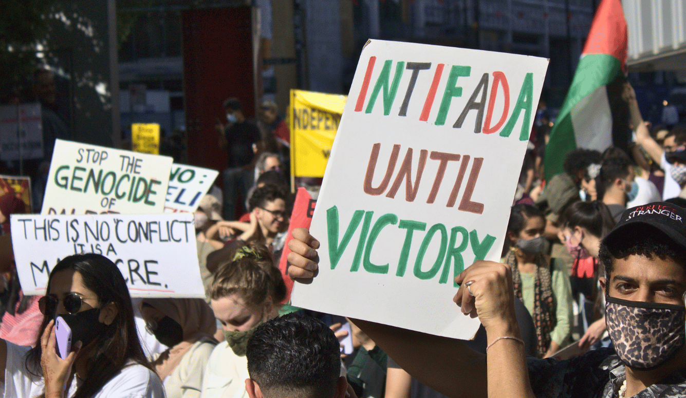Free Palestine protestors. One holds a banner stating INTIFADA UNTIL VICTORY. 