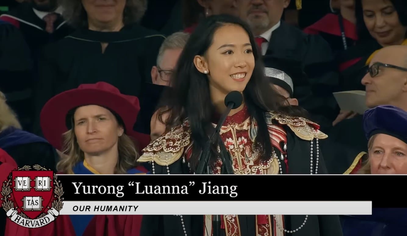 Jiang Yurong is a young East Asian woman. She stands at a microphone, smiling, wearing academic robes and traditional Chinese garb. 