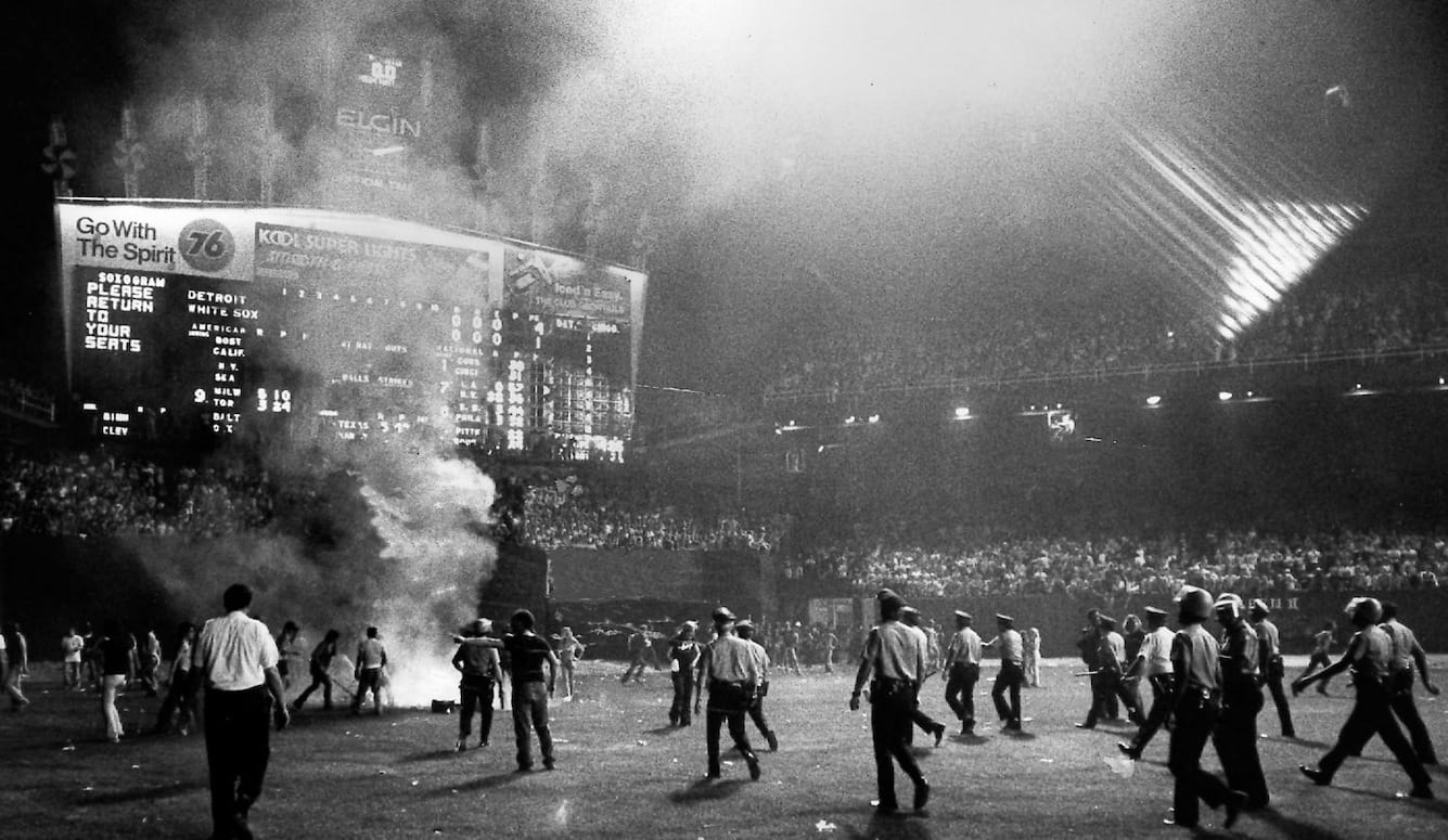 Black and white photo of crowd on a football ground. A fire is burning. Police move towards the scene. 