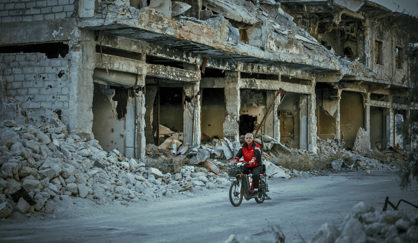 Man rides bike through rubble in Syria after war. 