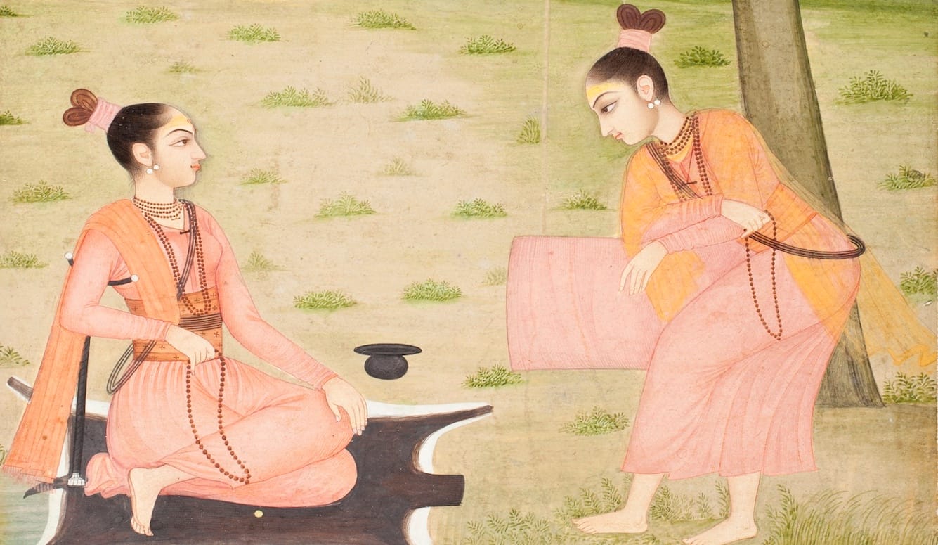 Two yoga practitioners, in traditional Indian garb. One sits on what appears to be a mat, the other bows. 