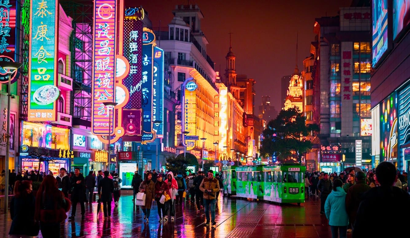 A colourful night-time street scene in China, with crowds of people, neon lights, and a tram. 