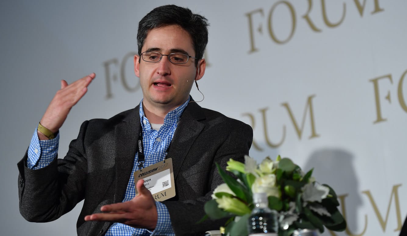 Oren Cass is a middle-aged man. He wears glasses and is speaking on stage, gesticulating. 
