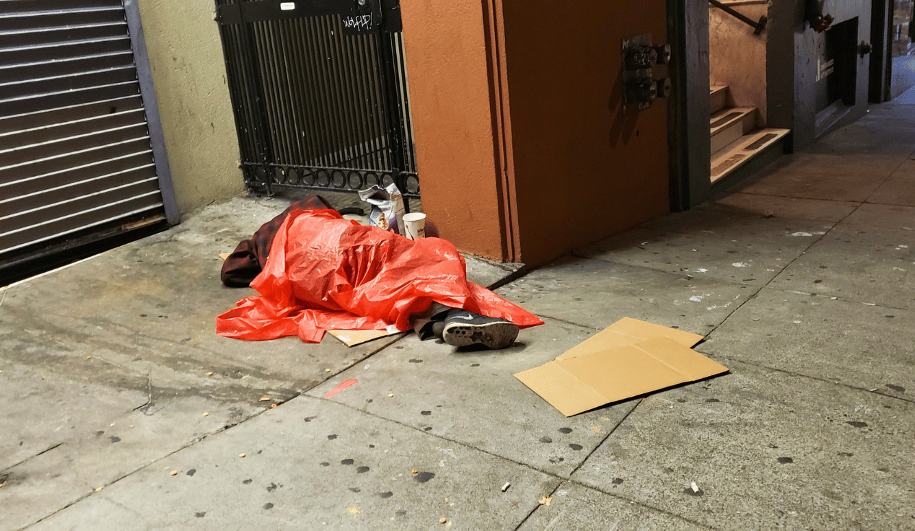 Homeless person wrapped in red plastic sheets on the sidewalk. 