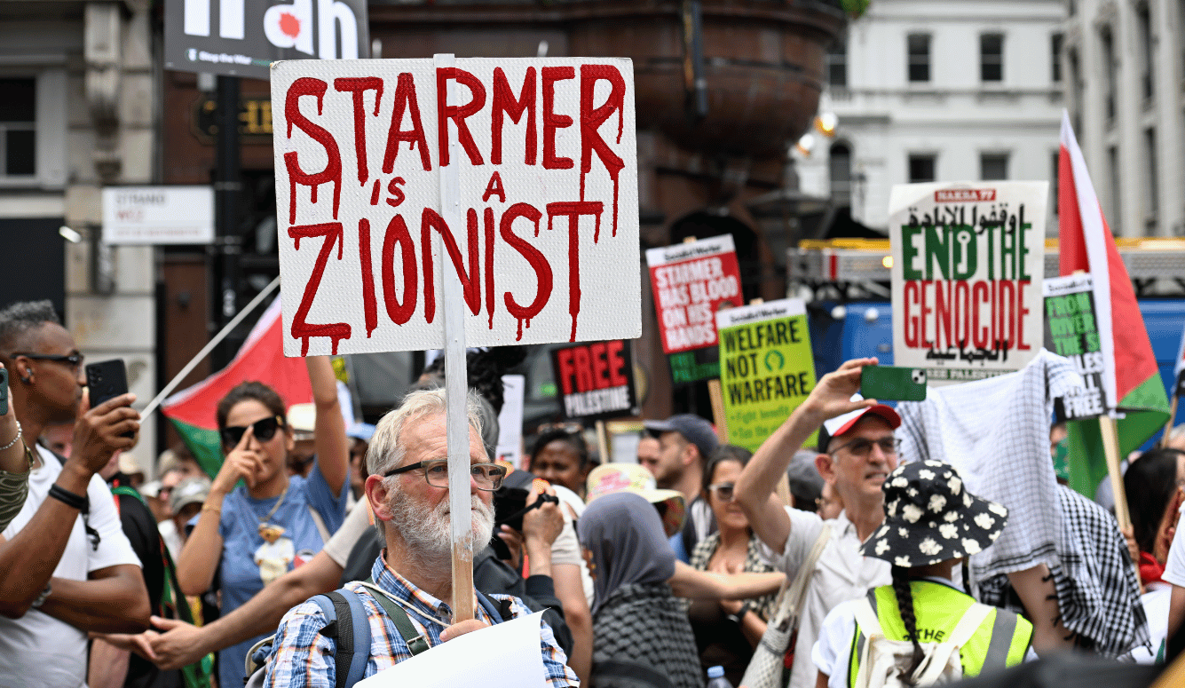 Pro Palestinian protester holding a sign saying "STARMER IS A ZIONIST" in blood-like ink