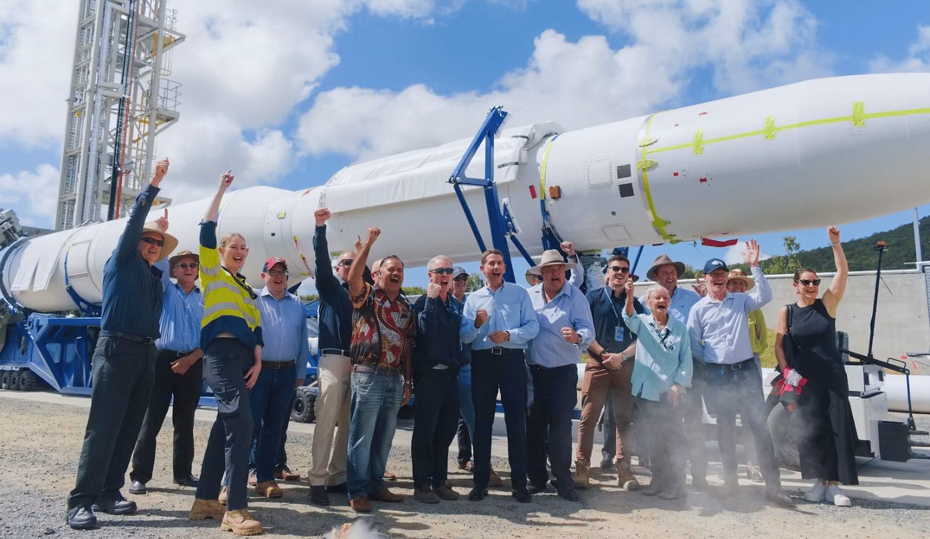 A crowd cheers in front of a space rocket.