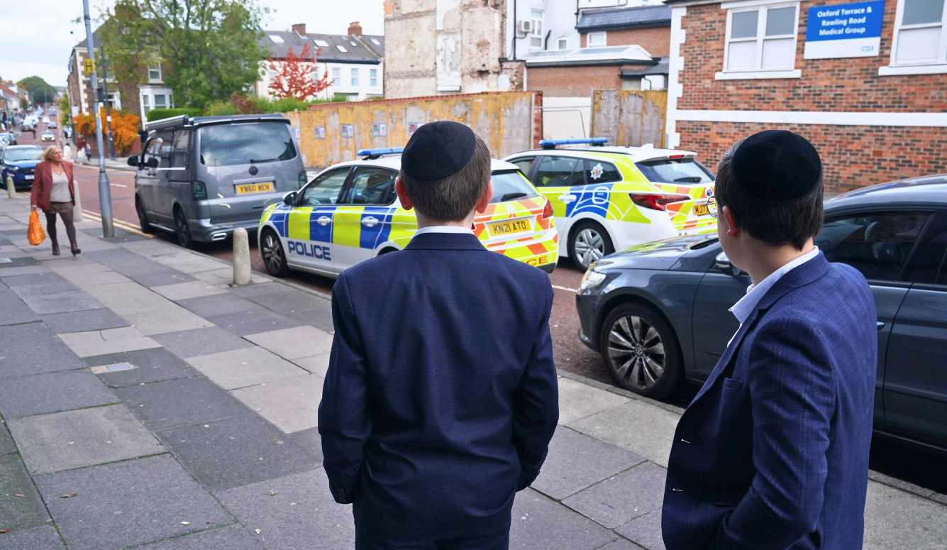 Young members of the Jewish community look at police cars close to the synagogue in Manchester.
