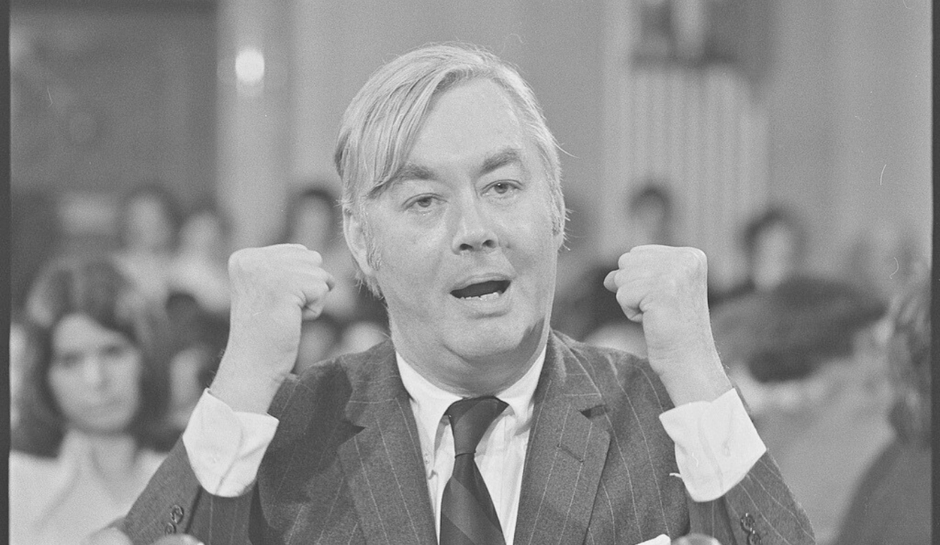 Daniel Patrick Moynihan, head-and-shoulders portrait, speaking behind microphones, gesturing with his hands, probably at a meeting of the Senate Committee on Foreign Relations