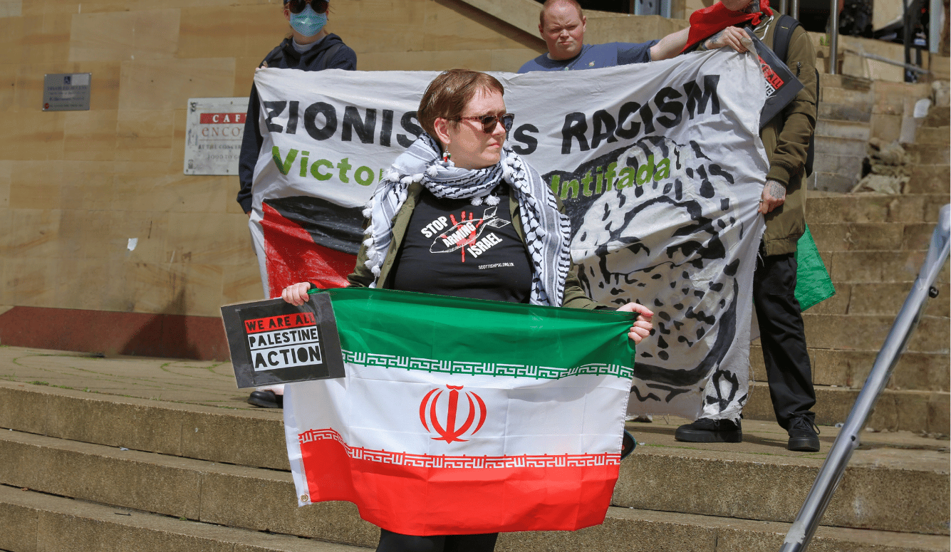 Protesters hold pro-Palestinian banners and an Iranian flag, including one reading “Zionism Is Racism—Victory to the Intifada.”