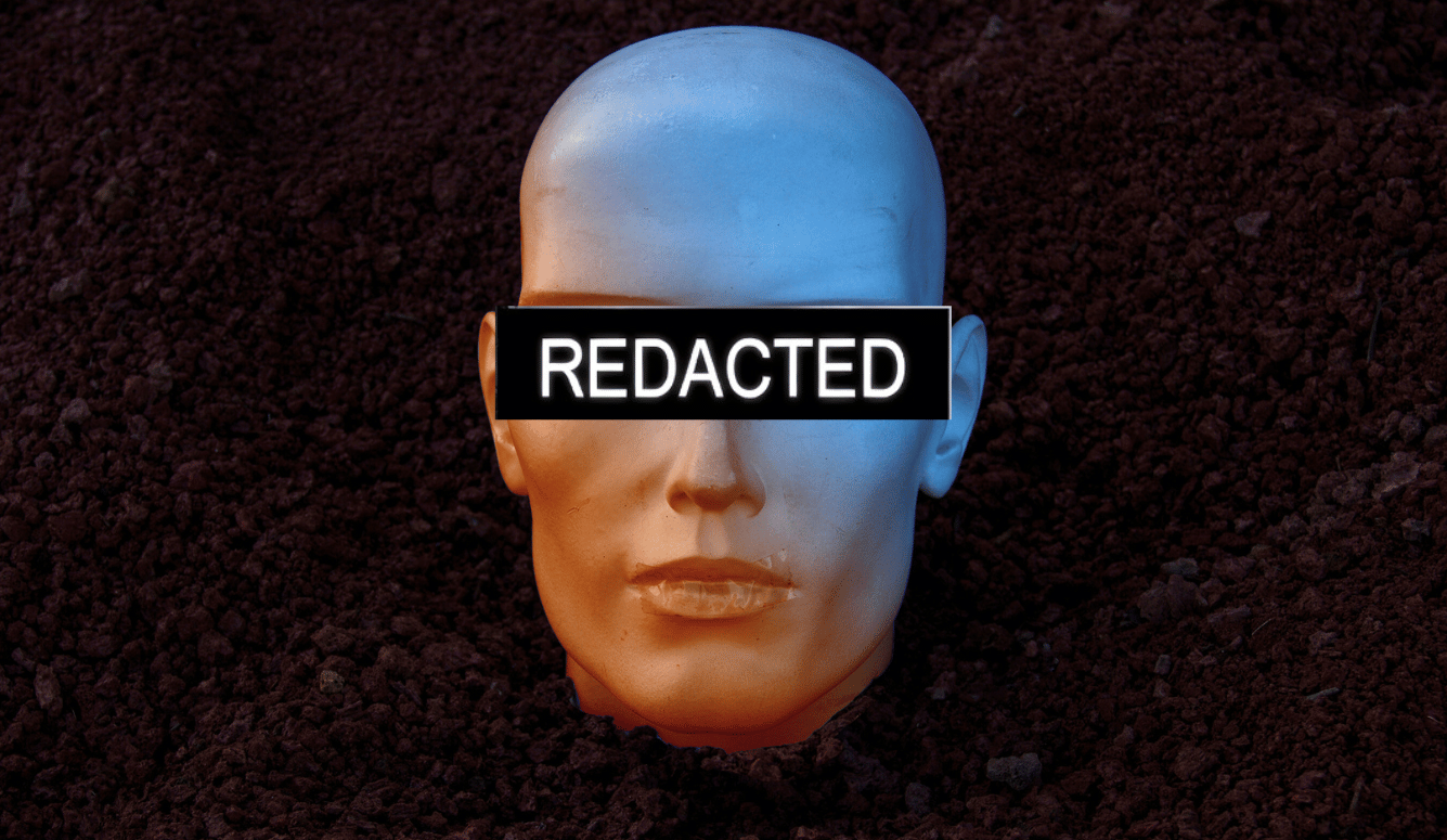 Plastic mannequin head half-buried in soil with a black bar reading “REDACTED” over the eyes.
