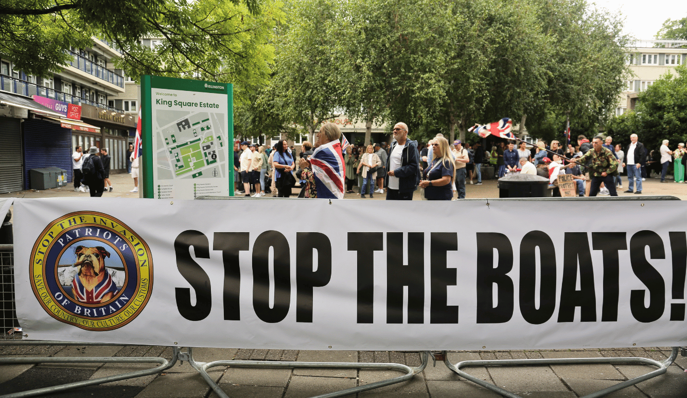 Protesters with Union Jack flags stand behind a “Stop the Boats!” banner at King Square Estate in Islington.