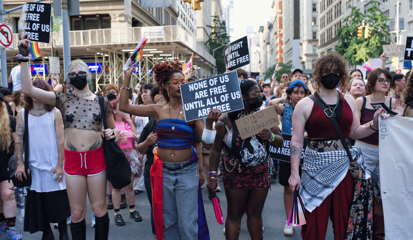 Protesters holding signs reading "NONE OF US ARE FREE UNTIL ALL OF US ARE FREE."