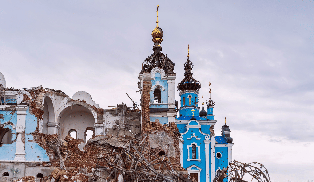 Ruined blue Orthodox church with damaged domes and collapsed masonry against an overcast sky.