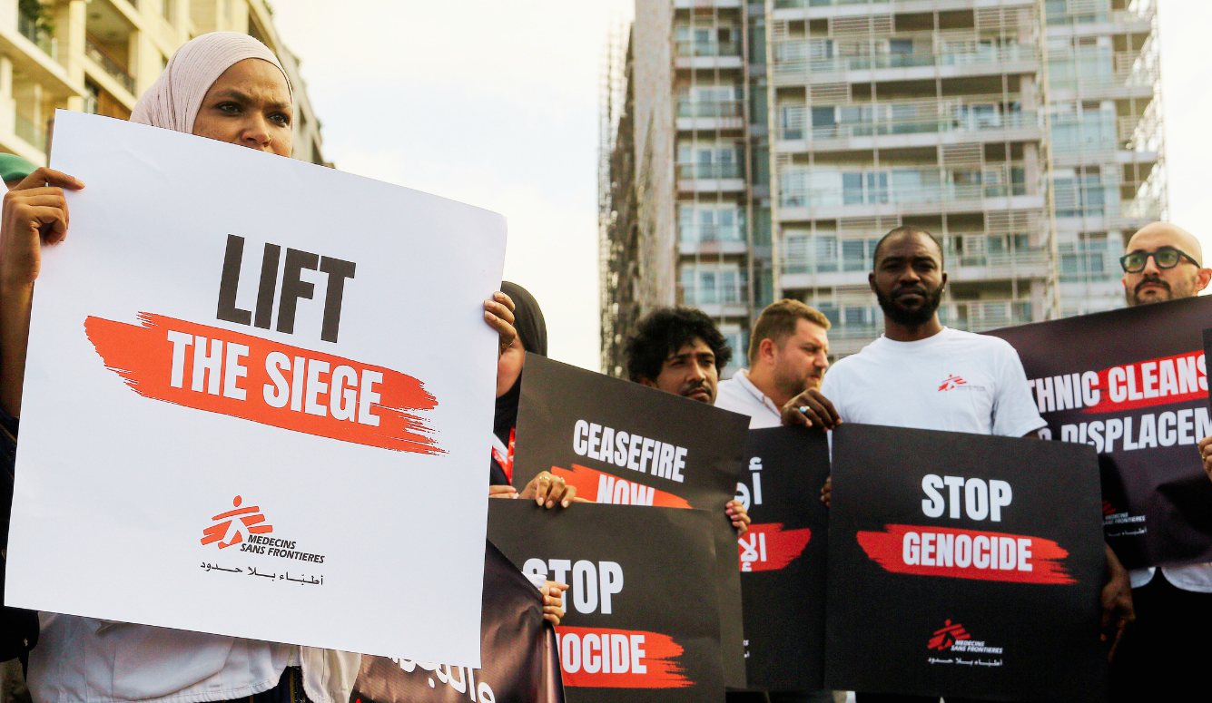 People holding protest signs calling for a ceasefire and an end to siege and genocide in an urban setting.