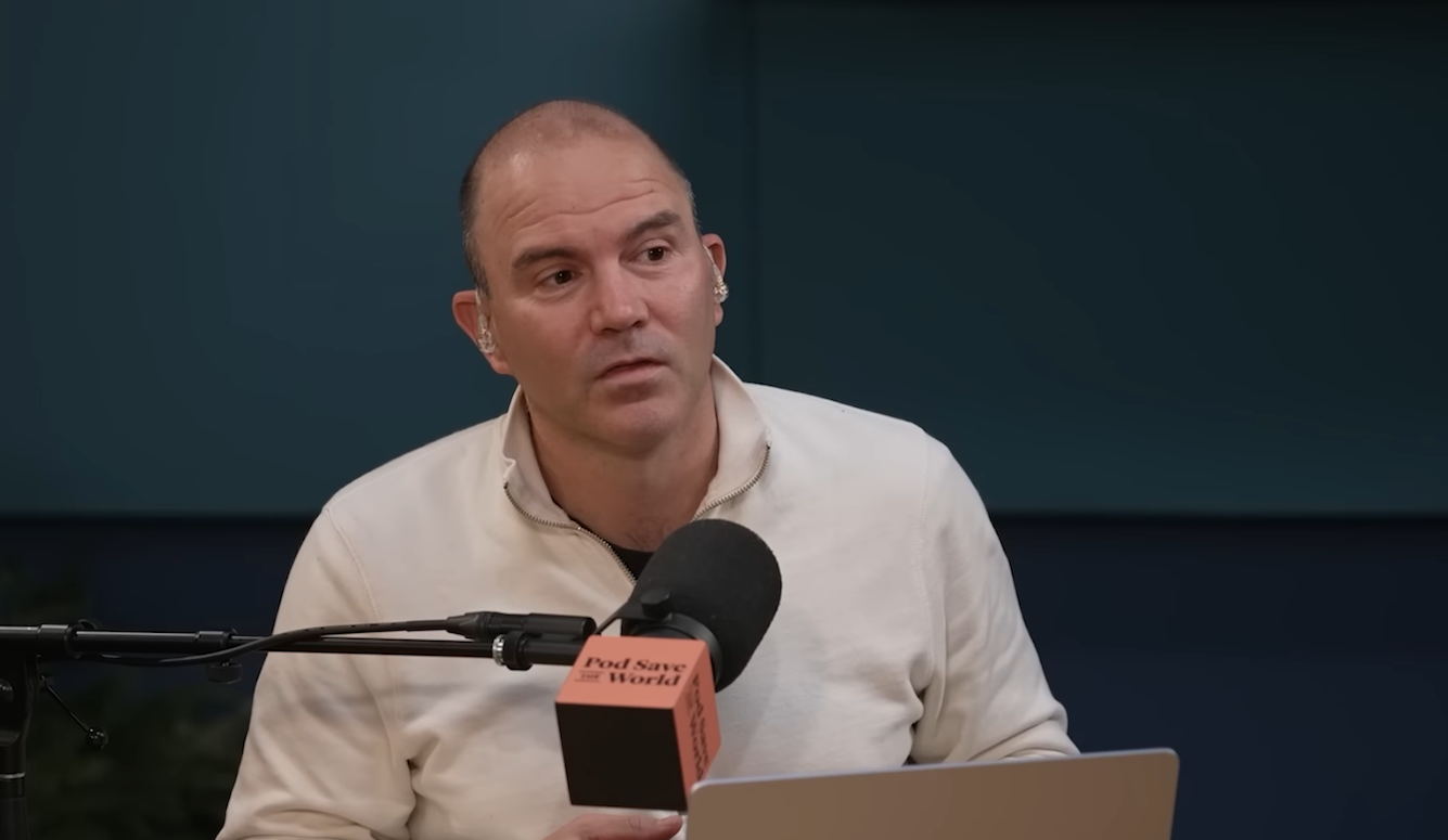 Ben Rhodes is a middle-aged white man. He is sitting a microphone labelled Pod Save the Worl