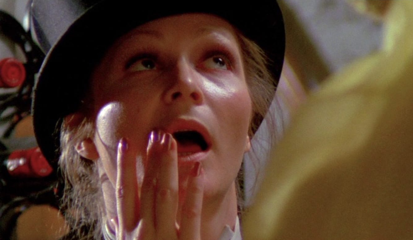 A close-up still from the movie Naked Came the Stranger, focusing on the lead actress’s face. She looks up, mouth open.