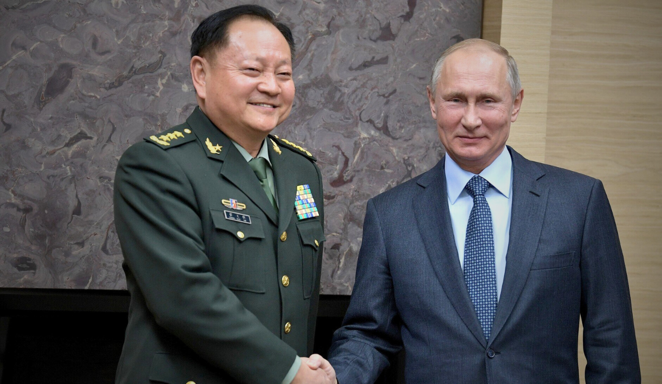 General Zhang Youxia, smiling, in dress uniform, shakes the hand of Vladimir Putin, who wears a suit and tie.  