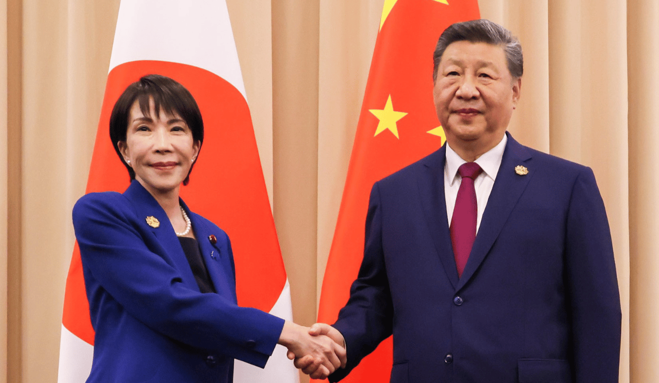 Japanese and Chinese leaders shake hands before Japanese and Chinese flags during a formal diplomatic meeting.