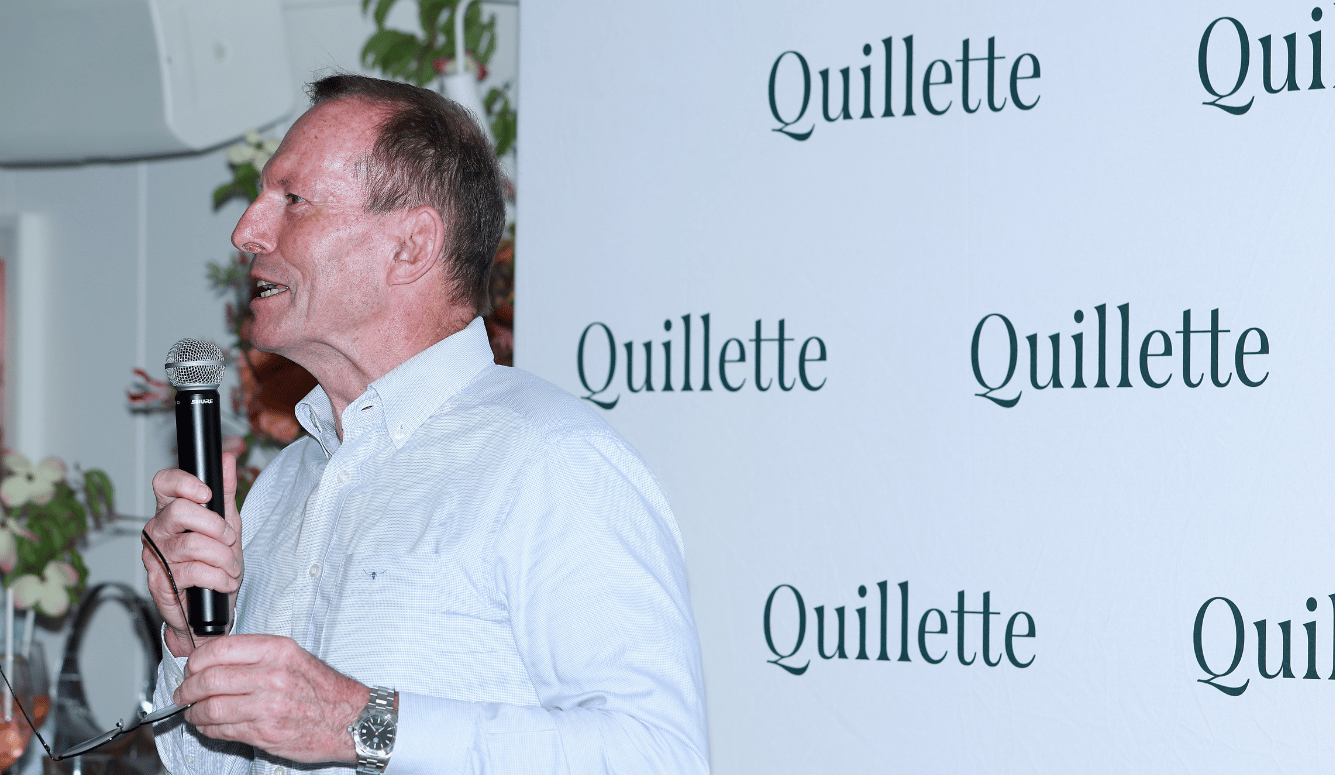 Tony Abbott speaks into microphone in front of Quillette sign.