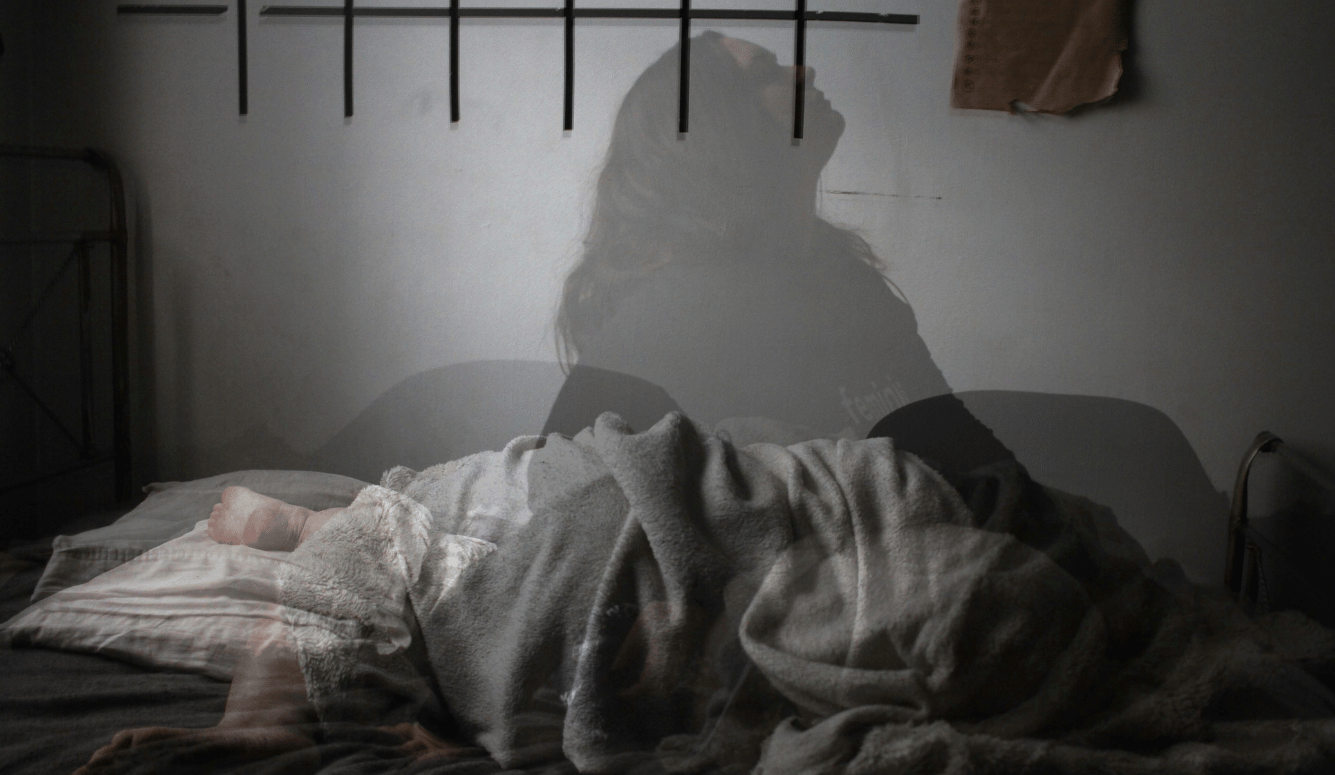 Double exposure of adult with long hair in bed under blanket, silhouette on wall in dim bedroom. 