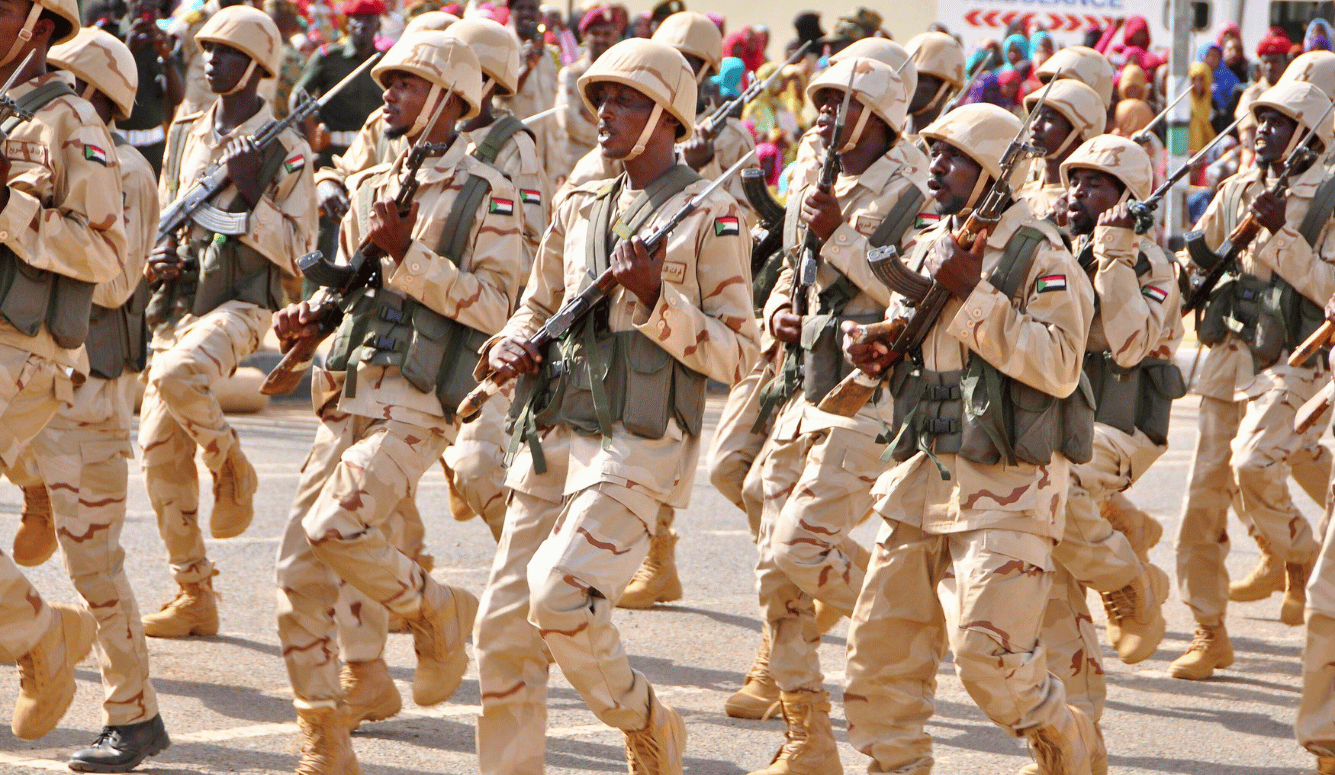 Sudanese soldiers in desert camouflage uniforms and helmets march with rifles during a military parade.