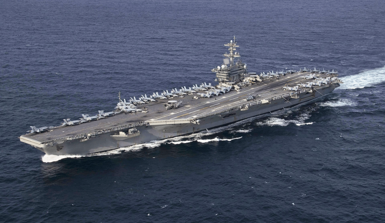 USS Abraham Lincoln, a large grey aircraft carrier, on blue water.