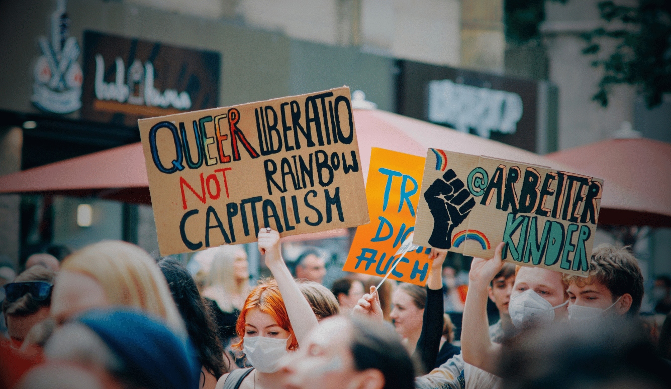 Protesters in face masks hold placards reading Queer Liberation Not Rainbow Capitalism and Arbeiter Kinder.