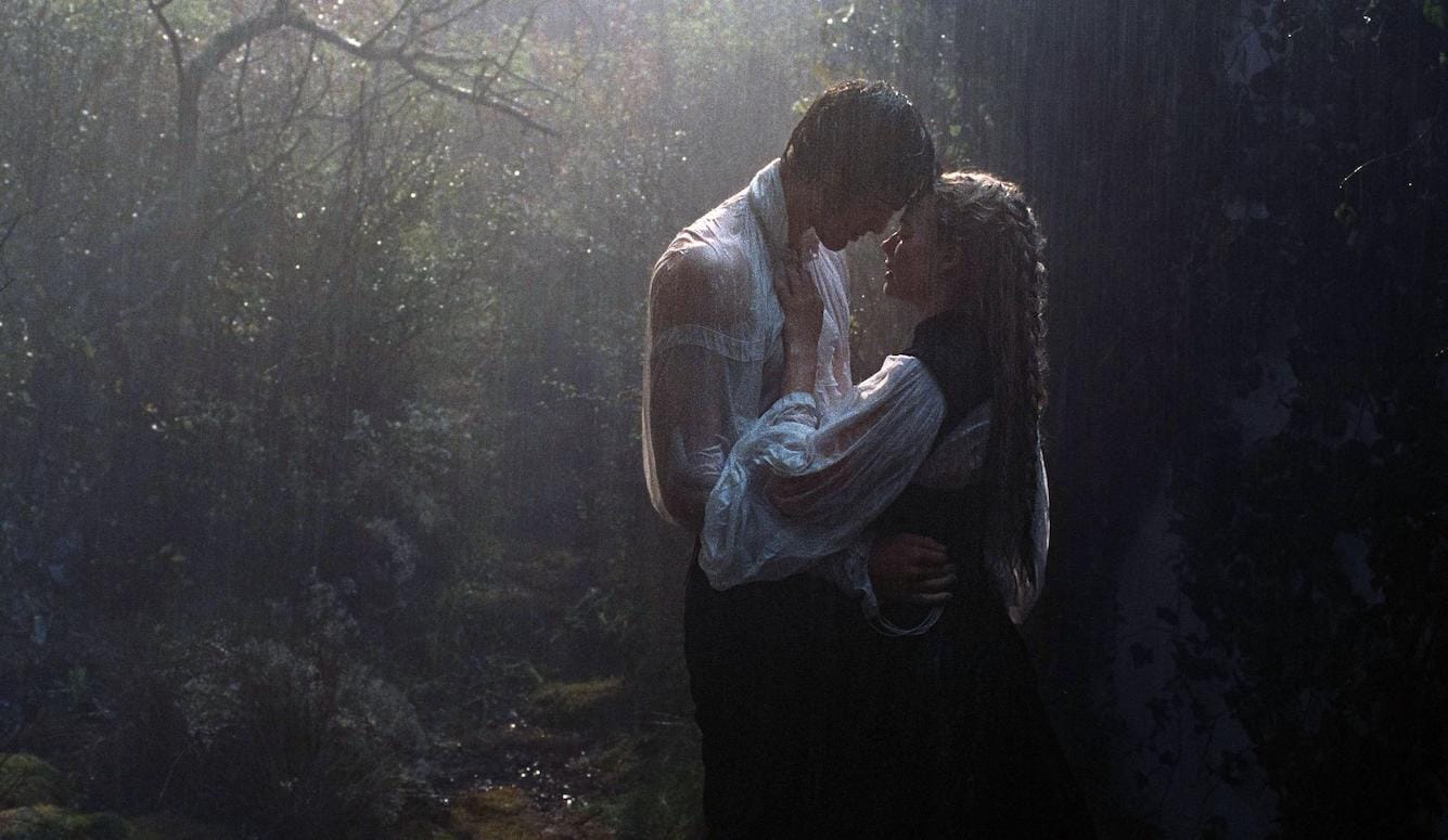 Two young people in a forest embracing in low lighting in period costume. 