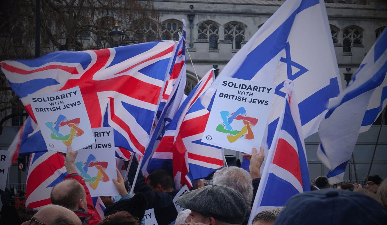 Protesters holding UK and Israeli flags and “Solidarity with British Jews” placards at antisemitism rally, Parliament Square, London, 2019.