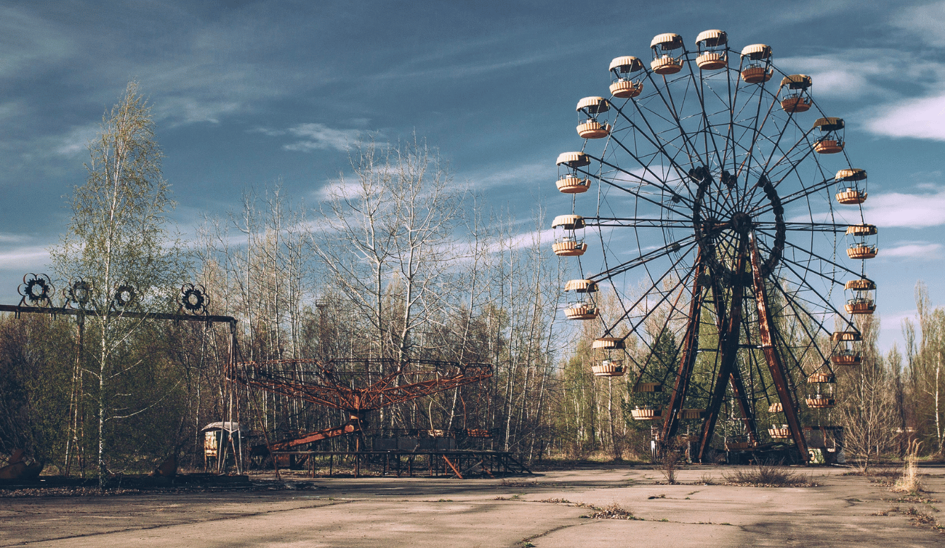 Abandoned fairground with ferry wheel and bare trees.