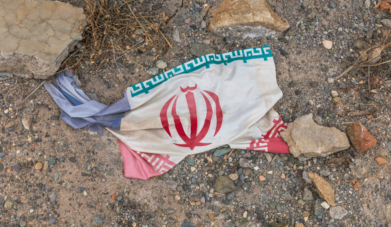 The flag of the Islamic Republic in Iran lies on the ground among rocks, as if discarded like lit