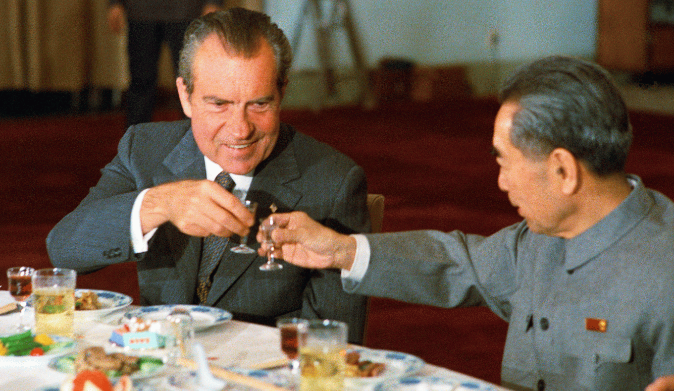 Zhou Enlai and Richard Nixon toast with small glasses at a formal Chinese banquet table; Nixon wears a Western suit, Zhou a grey Mao suit with a red pin.