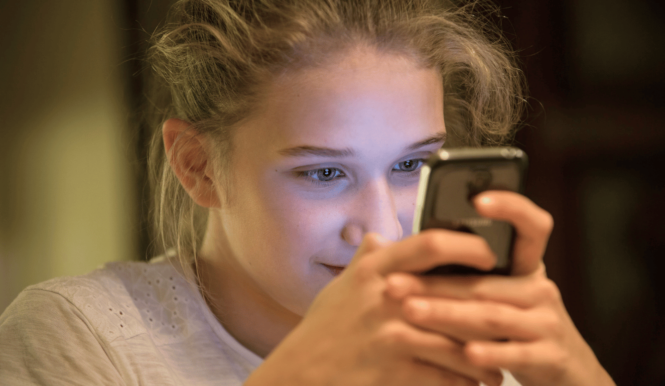 A young woman holds a mobile phone up to her face, her eyes intent on the screen. 