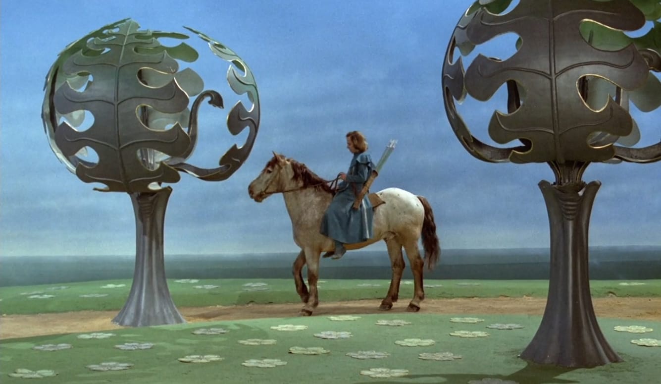 A young rider on horseback between two stylised sculptural trees in a surreal medieval landscape.