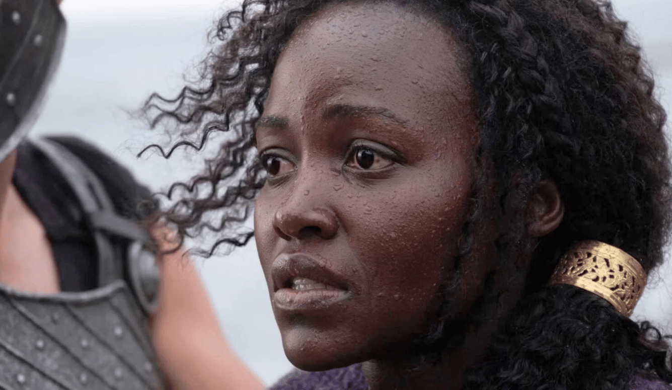 Close-up of Kenyan Lupita Nyong'o as Helen of Troy in battle armor, wet curly hair, intense expression. She has dark skin.