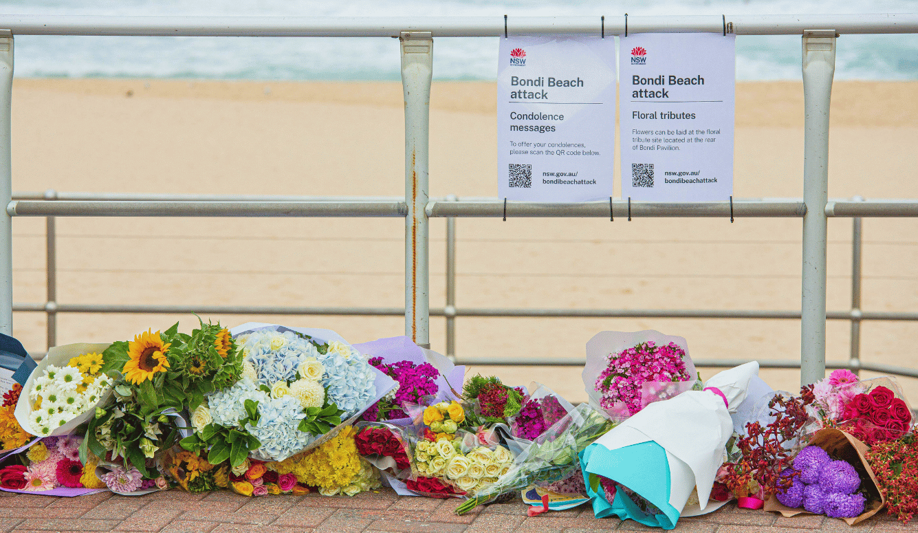 Bouquets of flowers and memorial tributes are laid along the promenade at Bondi Beach beneath notices inviting condolence messages.